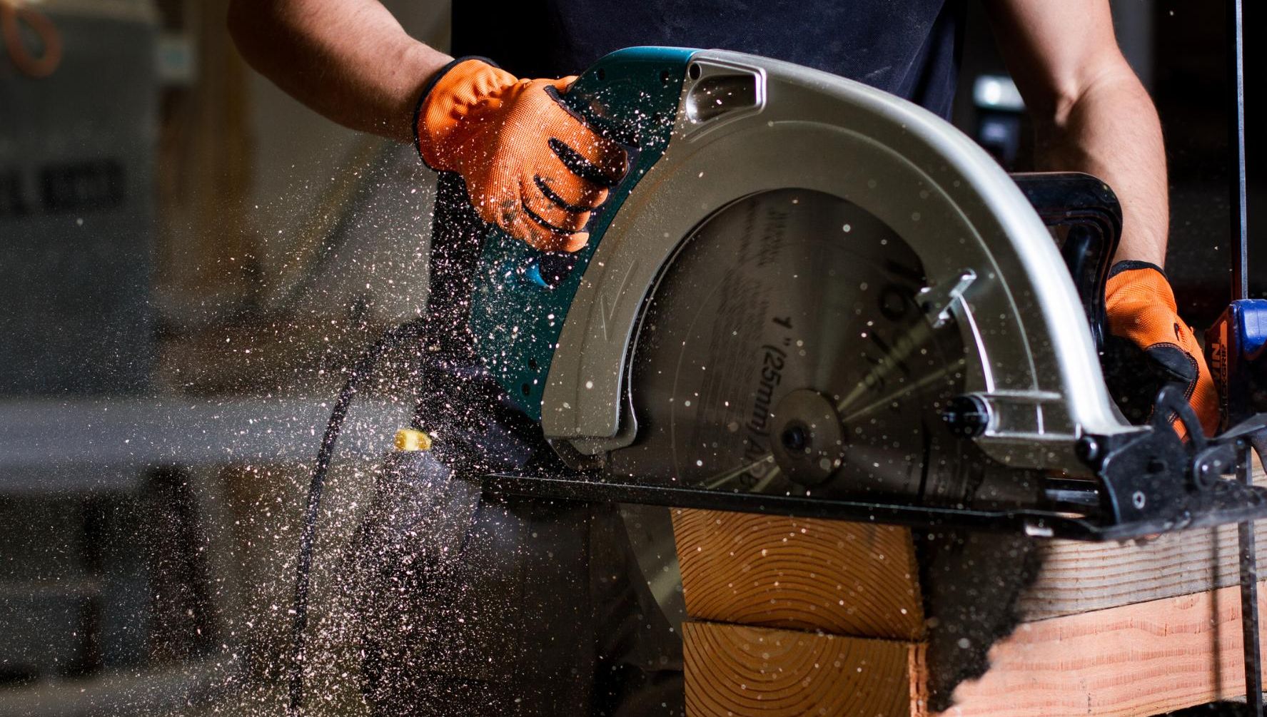Håndverker kapper trevirke med sirkelsag, sagflis spruter i verkstedmiljø