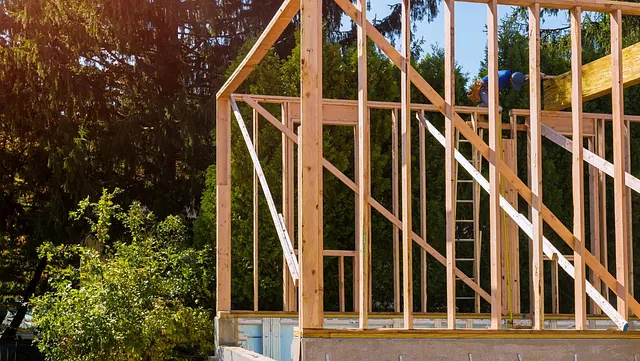 Trekonstruksjon til bolig under bygging, omgitt av trær og blå himmel