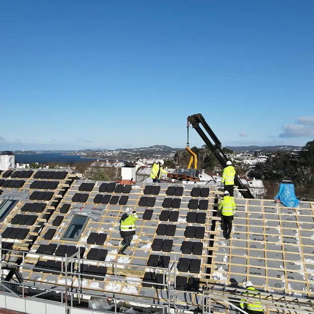 Takarbeidere i refleksvest monterer takstein