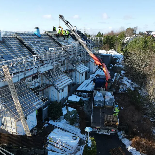 Takarbeidere monterer takstein på boligtak med kran og stillas i vinterlig boligområde